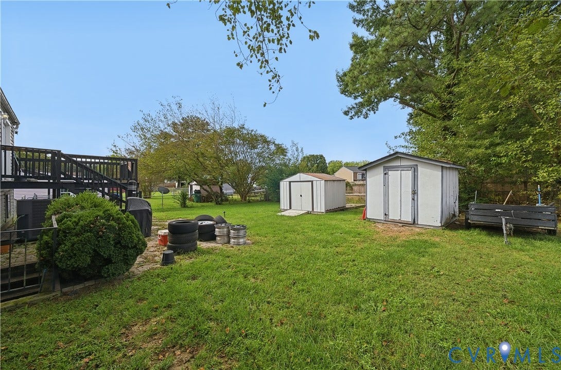 Expansive backyard featuring a manicured lawn, two storage sheds, and a raised wood deck