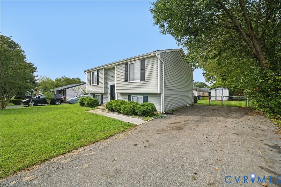 Split-level exterior with light-colored siding, contrasting dark shutters, and a paved driveway