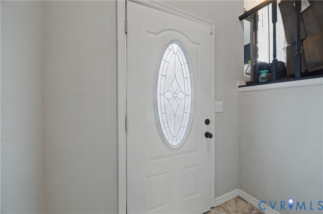 White paneled entry door with an oval decorative glass insert, black door hardware, and light-toned wall finishes