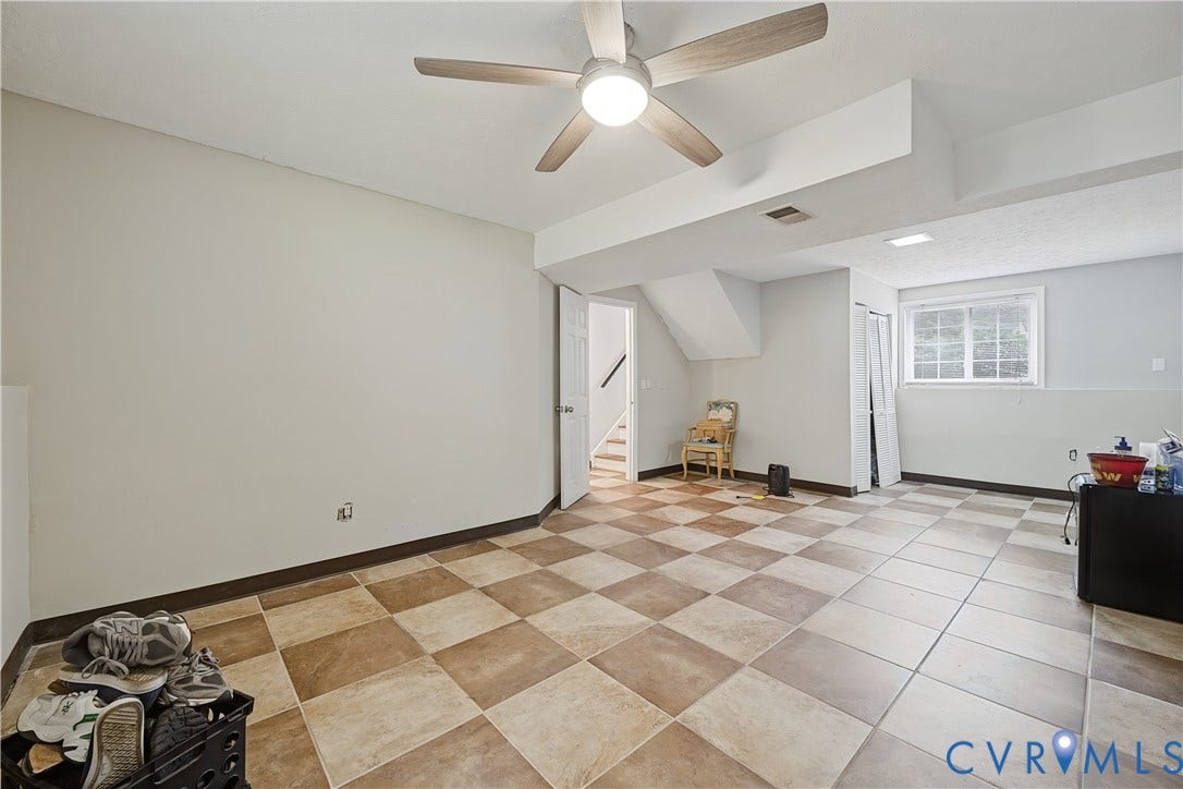 Spacious room featuring checkered tile flooring, a ceiling fan with integrated lighting, and a white-framed window