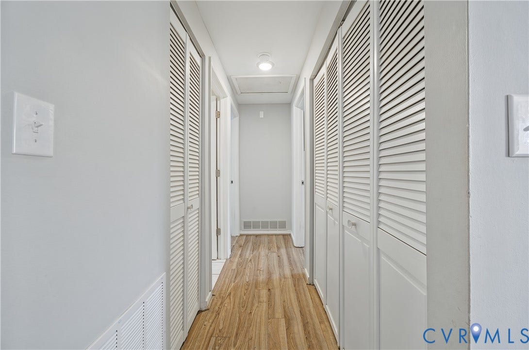 Hallway featuring wood-finish flooring, white louvered doors, and light gray wall paint