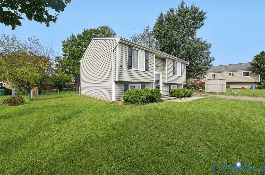 Split-level residence featuring light-colored siding, dark shutters, and a well-maintained lawn