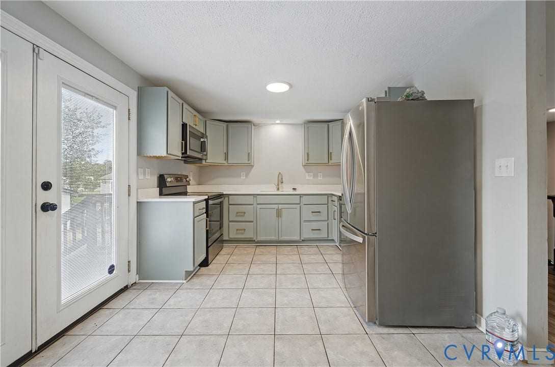 Kitchen featuring tile flooring, light-toned cabinetry, stainless steel appliances, and a full-light door