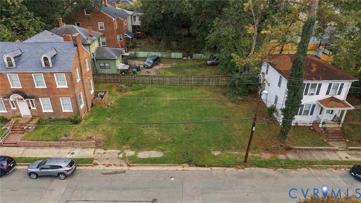 Expansive grassy lot featuring mature trees and a partial wood fence