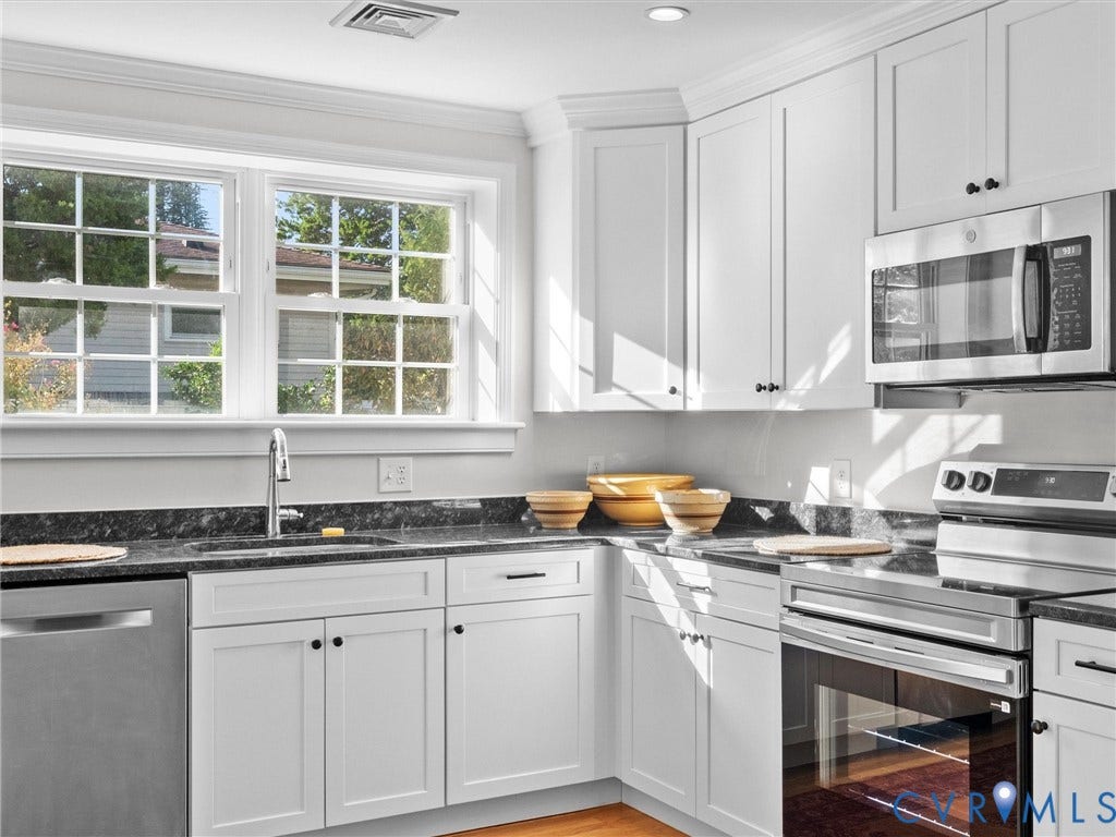 White shaker cabinetry, black stone countertops, stainless steel appliances, recessed lighting, and wood-finish flooring
