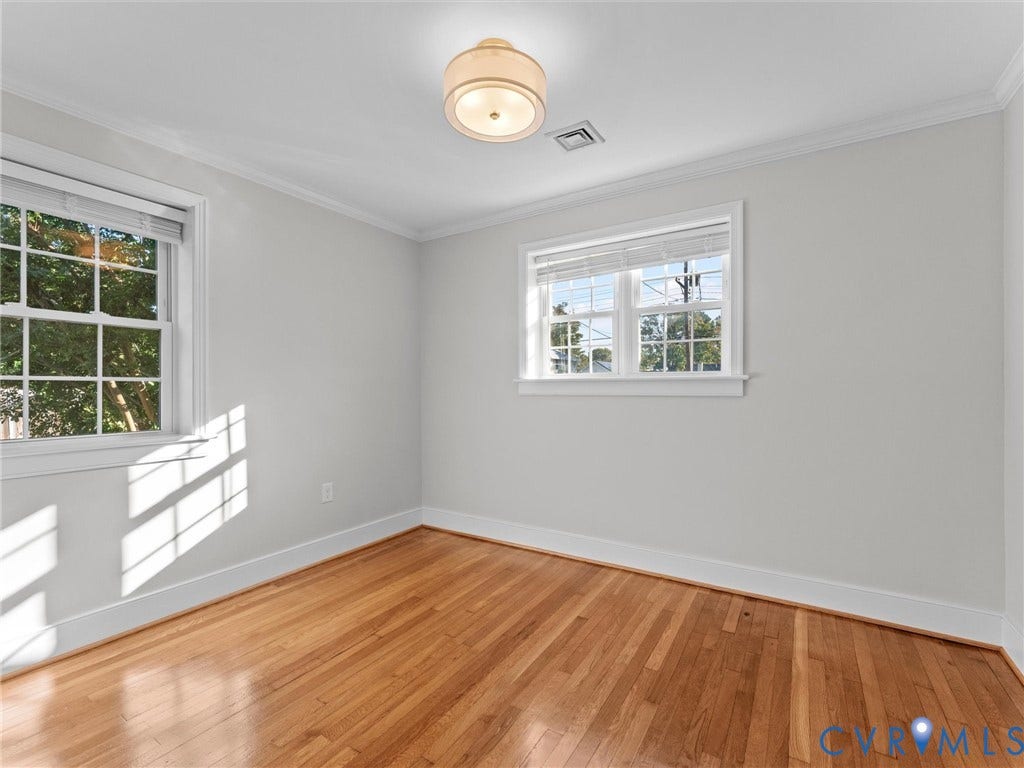 Hardwood flooring, two large windows, white trim, crown molding, and a ceiling-mounted light fixture