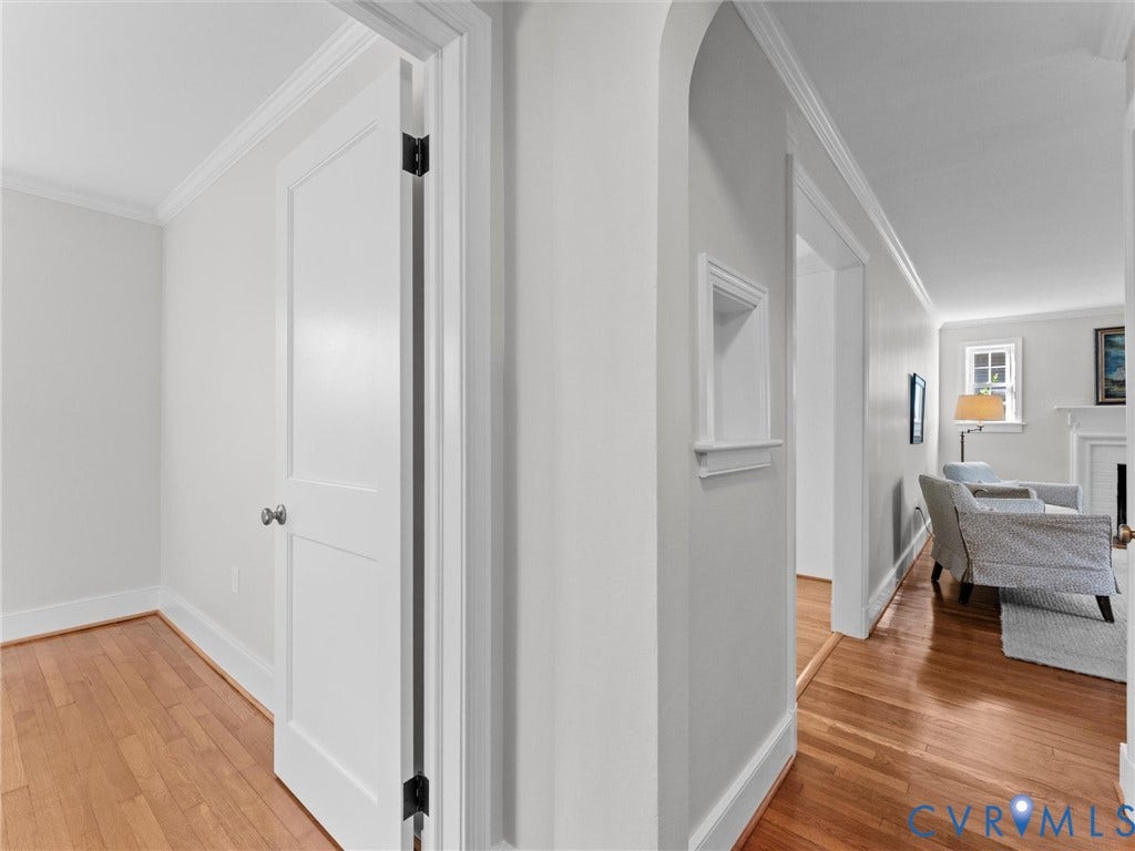 Hardwood flooring, painted interior door, arched entryway, crown molding, and a wall niche