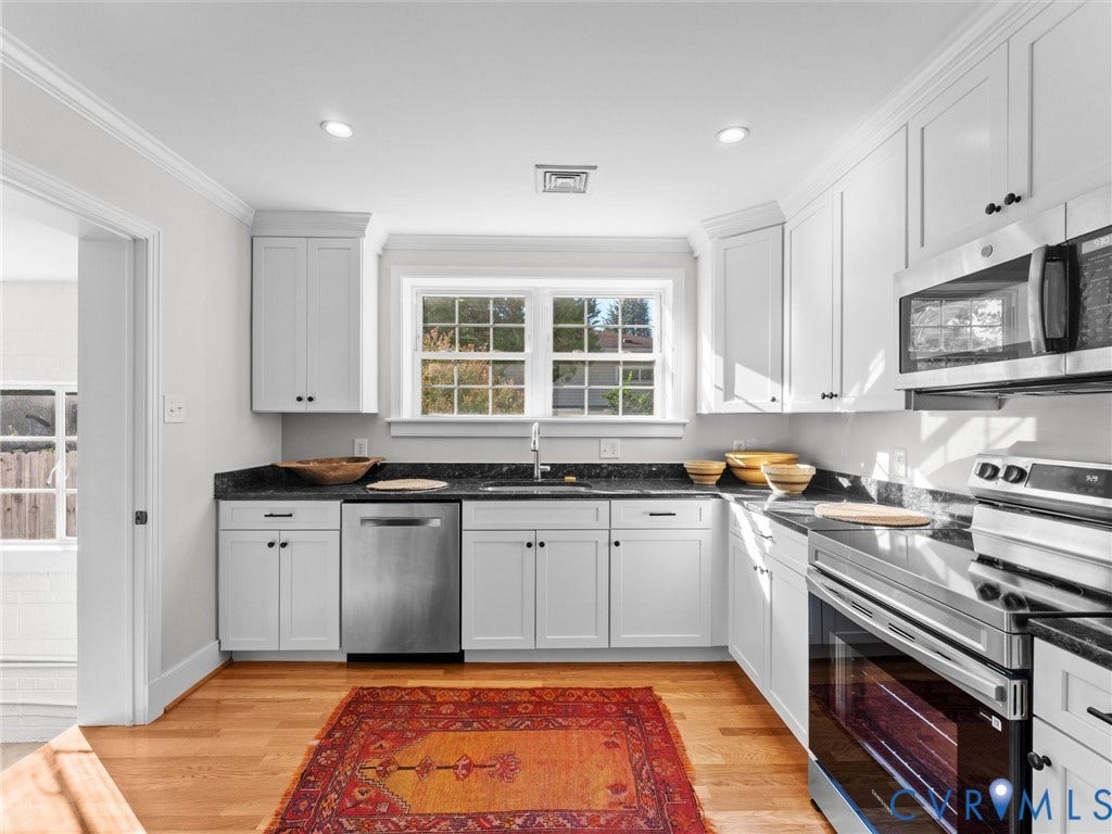 White cabinetry with black hardware, stainless steel appliances, dark stone countertops, wood-finish flooring, and recessed lighting