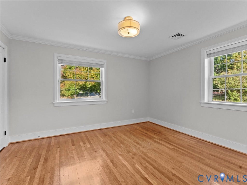 Hardwood flooring, crown molding, two windows with blinds, flush mount ceiling light fixture, and light gray wall paint