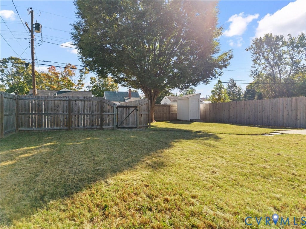 Expansive backyard with a large shade tree, wood privacy fencing, and a white storage shed