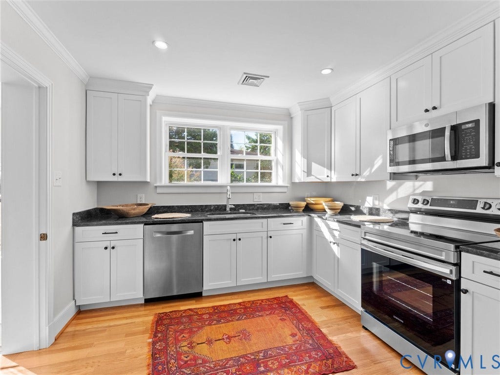 White cabinetry, dark stone countertops, stainless steel appliances, wood-finish flooring, and recessed lighting
