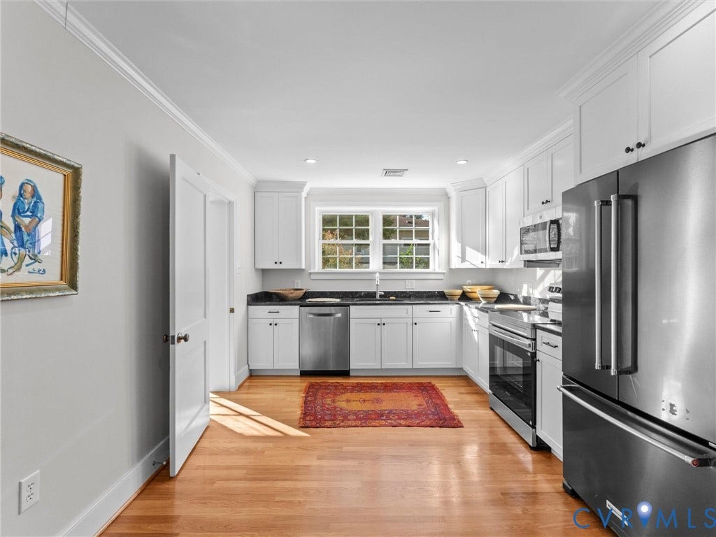 U-shaped kitchen with wood-finish flooring, white cabinetry, dark stone countertops, and stainless steel appliances