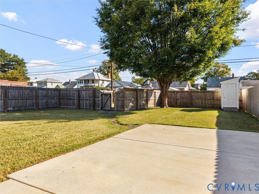 Expansive backyard featuring a privacy fence, concrete patio, a mature shade tree, and a storage shed