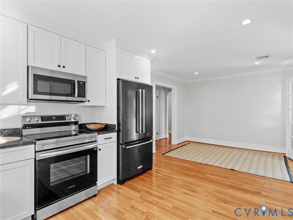 White shaker-style cabinetry, stainless steel appliances, dark stone countertops, wood flooring, and recessed lighting