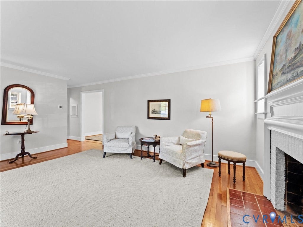 Hardwood flooring, fireplace with white mantel, tiled hearth, crown molding, and a wide doorway