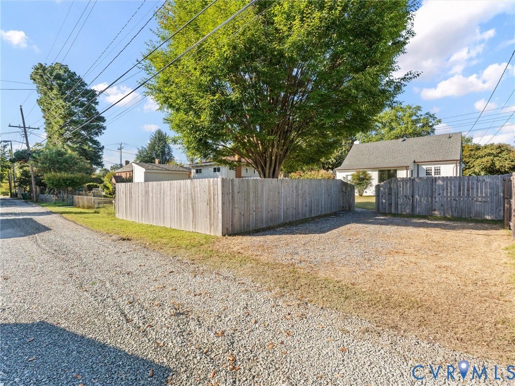 Gravel driveway leading to a fenced backyard with a mature tree and a residential structure