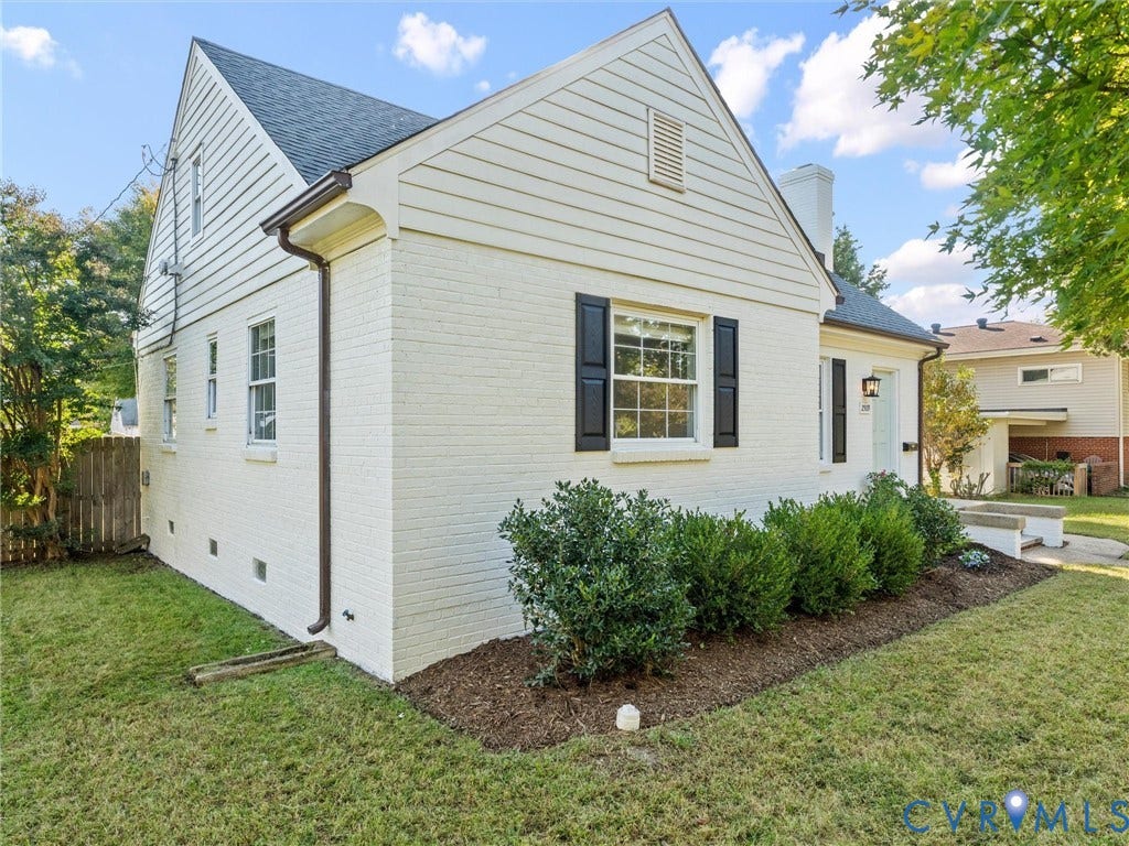 Brick and siding exterior with dark shutters, front door with transom window, landscaped front yard, and a paved walkway