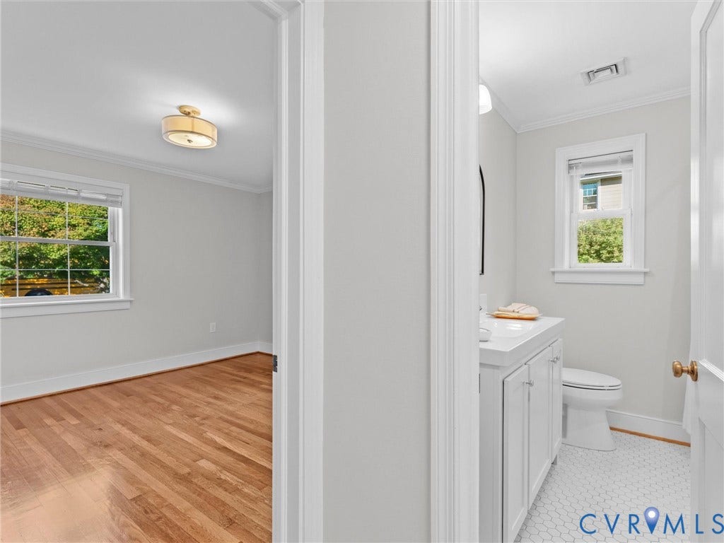 Refinished hardwood flooring, crown molding, double window, recessed lighting, and a bathroom with a white vanity and hexagon tile flooring