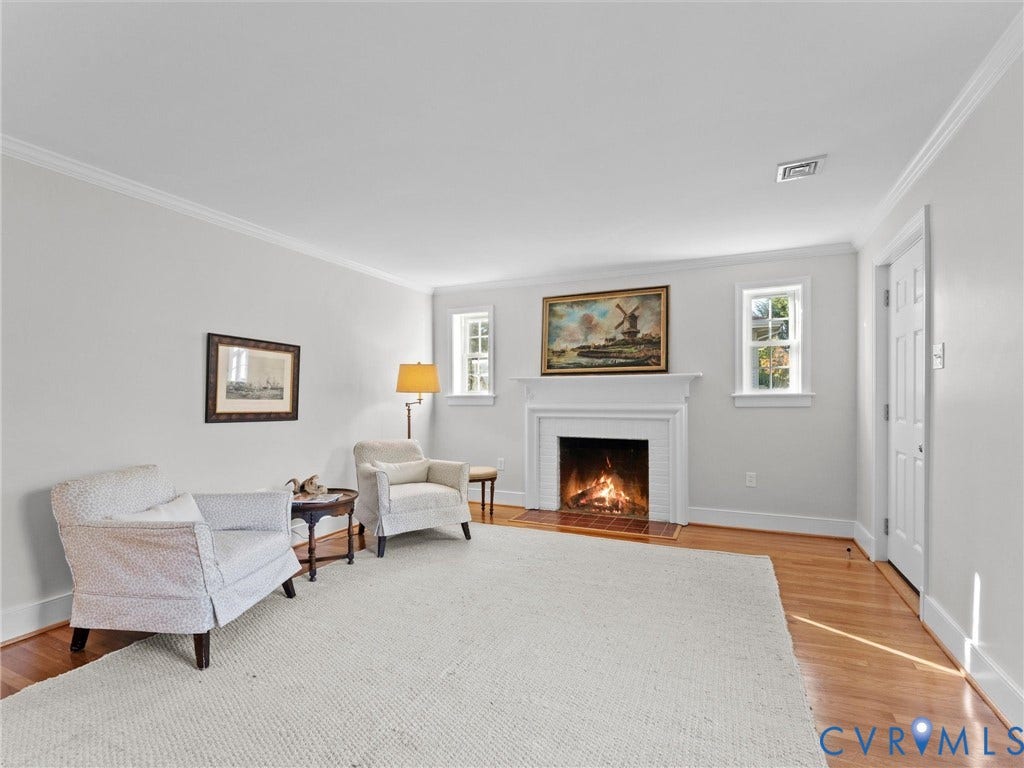 Hardwood flooring, crown molding, white trim, and a fireplace with a white mantel
