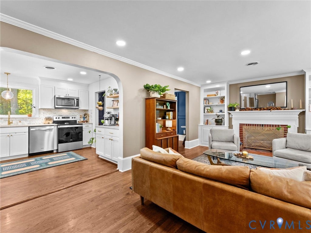 8341 Charlise Road, Stratford Hills, Midlothian, VA 23235 Open-concept kitchen featuring white cabinetry, stainless steel appliances, and wood-finish flooring, centered by an arched transition to the living area with a fireplace and built-in shelving