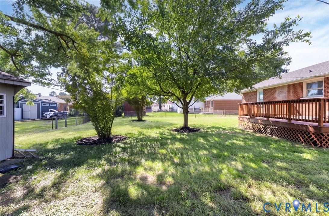 2211 Apollo Road, Fairfield, VA 23223 Expansive backyard featuring a manicured lawn, established trees, and a wooden deck with lattice skirting