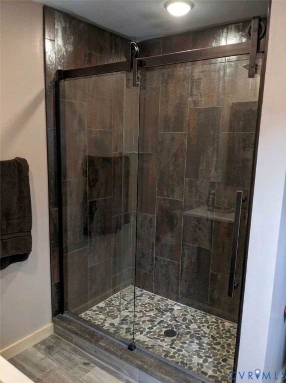 Frameless glass shower enclosure with a barn door style hardware system, pebble tile shower floor, and large format wall tiles