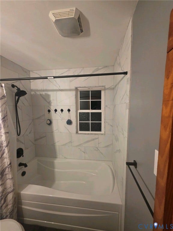 Bathtub with white subway tile surround, black shower fixtures, and a window with divided lites