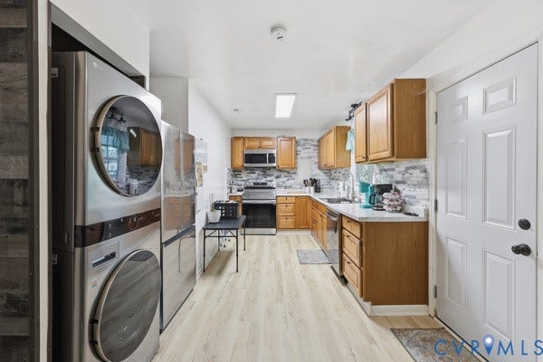 4647 Twelveoaks Road, Midlothian, VA 23112 Kitchen featuring wood cabinetry, stone-style tile backsplash, light-toned wood-finish flooring, and stainless steel appliances including a built-in microwave and stacked laundry unit