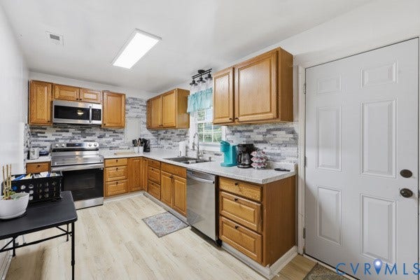 4647 Twelveoaks Road, Midlothian, VA 23112 Kitchen featuring wood cabinetry, stone-texture backsplash, stainless steel appliances, light-toned wood-finish flooring, and solid-surface countertops