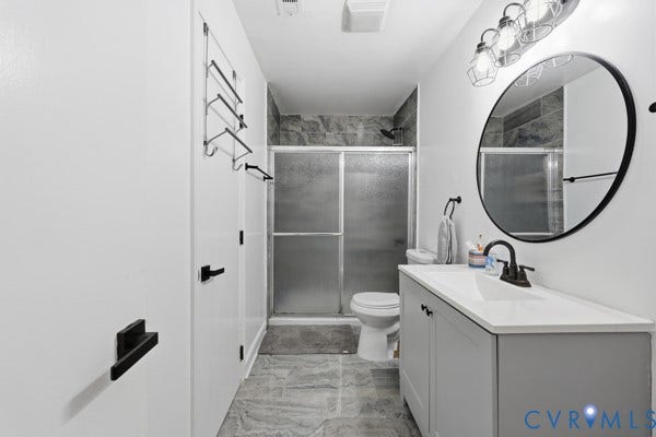 4647 Twelveoaks Road, Midlothian, VA 23112 Bathroom featuring a grey vanity cabinet with a white countertop, circular mirror with a black frame, matte black hardware, and a walk-in shower with stone-patterned tile surrounds