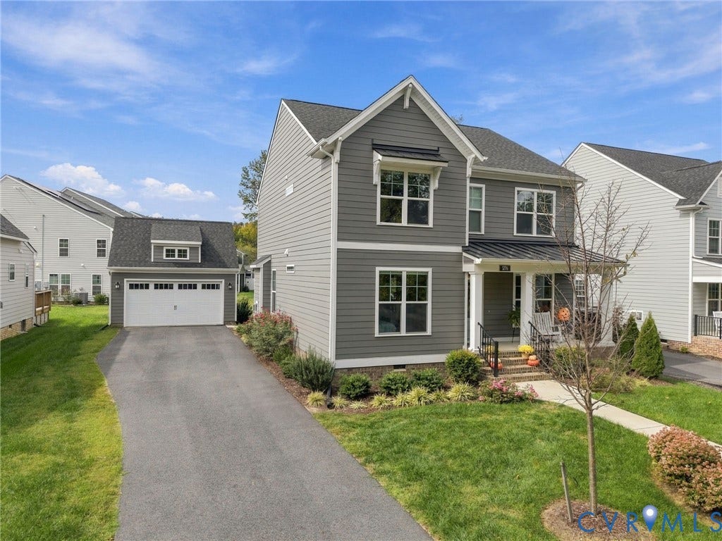 Gray siding exterior with white trim, covered front porch, asphalt driveway, detached two-car garage with dormer, and landscaped front yard