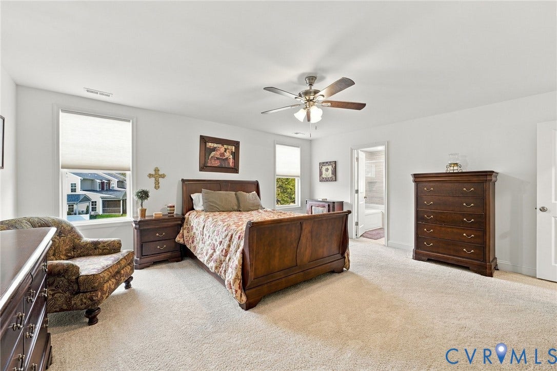 Spacious room featuring carpeting, multiple windows with blinds, a ceiling fan with integrated lighting, and a white paneled door