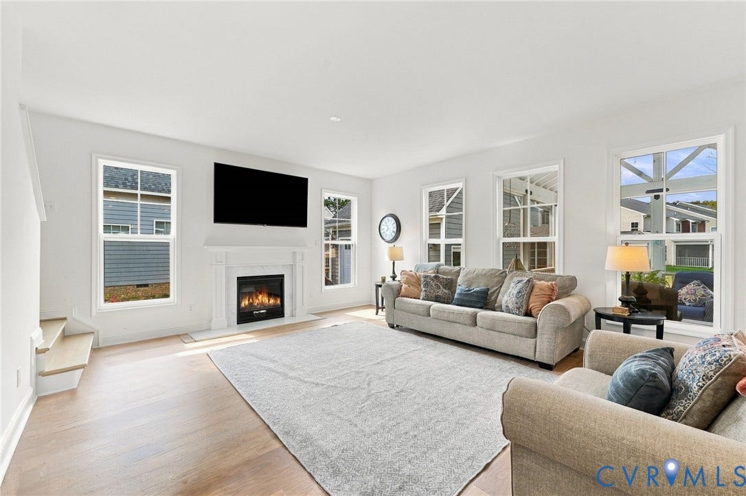 Living area featuring light wood-finish flooring, multiple windows, a decorative fireplace with a mantel, and recessed lighting