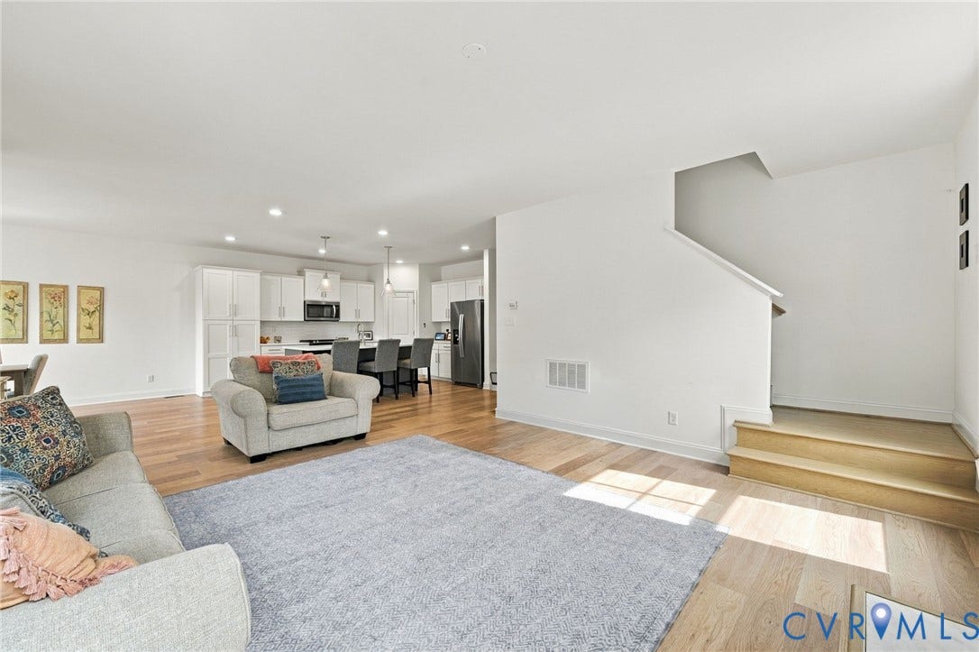 Open-concept living space featuring wood-finish flooring, recessed lighting, a staircase with wood treads, and an adjacent kitchen with white cabinetry and stainless steel appliances