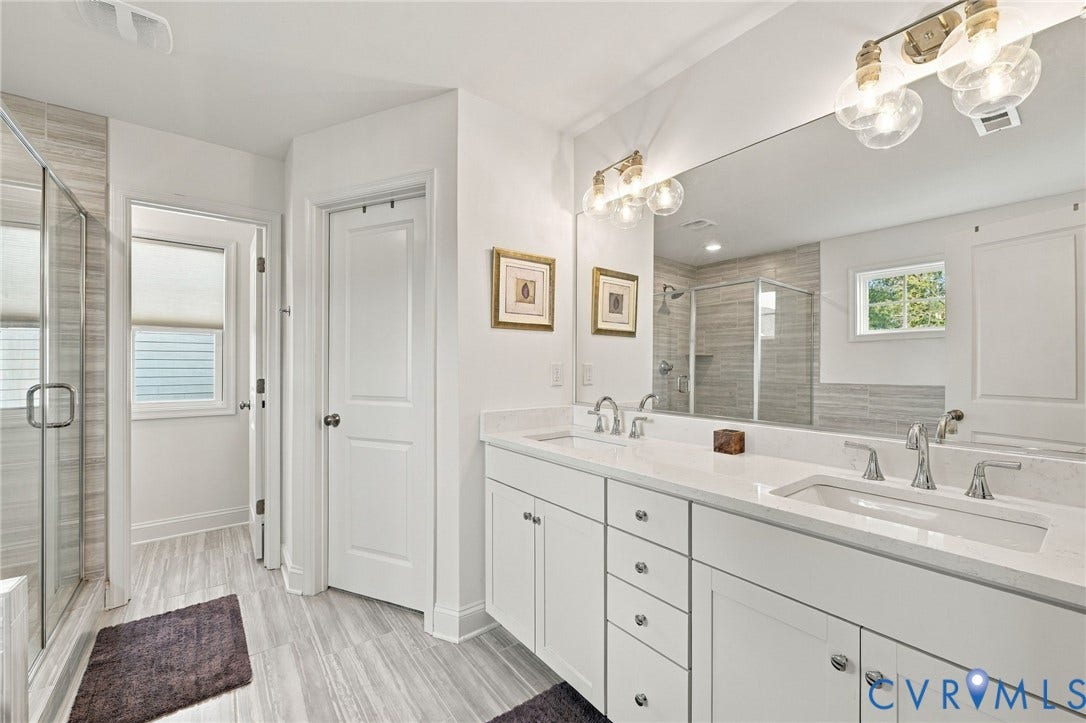 Dual vanity with white cabinetry and integrated sinks, a large mirror, and glass-enclosed shower with tile surround
