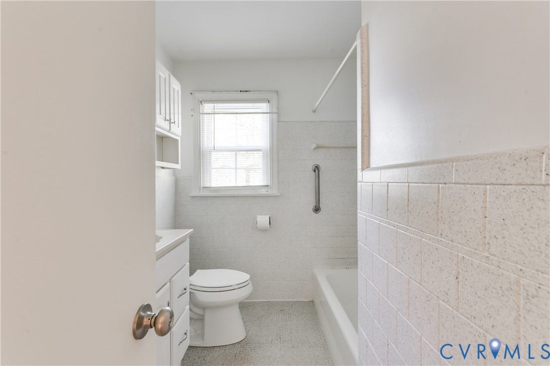 1701 Kingswood Street, Richmond, VA 23224 Bathroom featuring white wall-mounted cabinetry, a bathtub with a tiled surround, a mounted grab bar, and a single-hung window