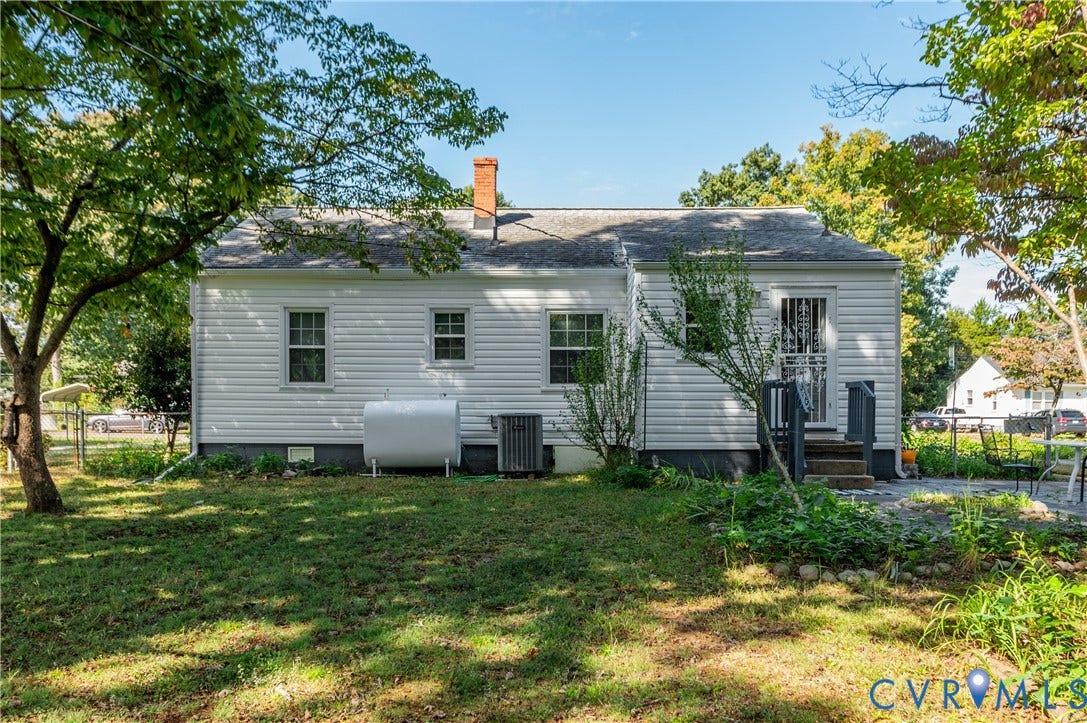 1701 Kingswood Street, Richmond, VA 23224 Exterior rear elevation featuring white horizontal siding, a central brick chimney, a multi-pane glass-panel door, and a paved patio area