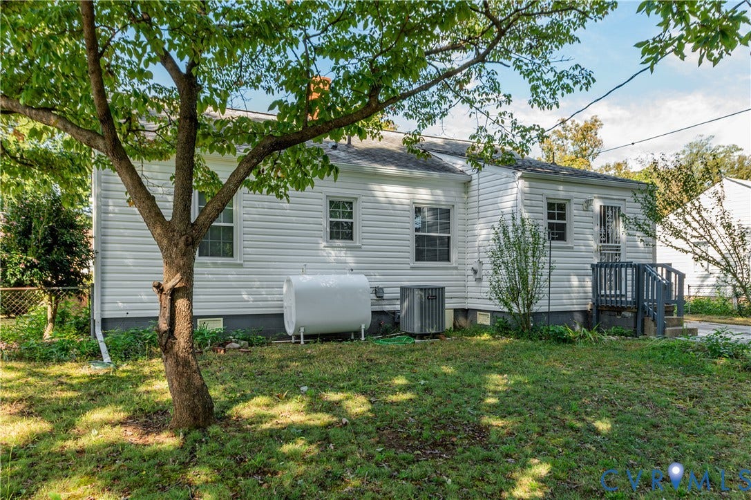 1701 Kingswood Street, Richmond, VA 23224 Exterior featuring white vinyl siding, a rear entry with wooden steps, mature trees, and a ground-level propane tank