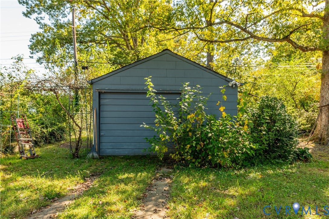 1701 Kingswood Street, Richmond, VA 23224 Detached garage with gray siding, metal overhead door, gable roofline, and paved driveway path