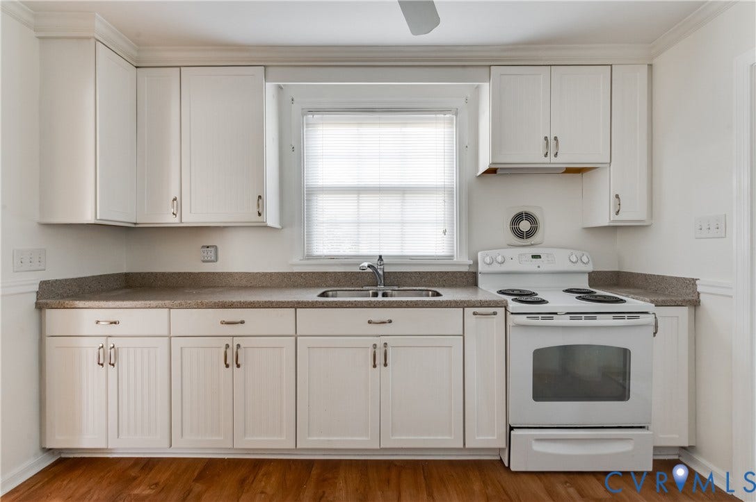 1701 Kingswood Street, Richmond, VA 23224 Kitchen featuring white shaker-style cabinetry, neutral-toned solid surface countertops, a stainless steel double-basin sink, and wood-finish flooring