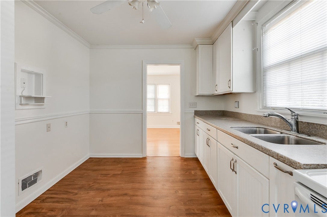 1701 Kingswood Street, Richmond, VA 23224 Kitchen featuring white cabinetry, solid-surface countertops, dual-basin stainless steel sink, and wood-finish flooring with chair rail molding