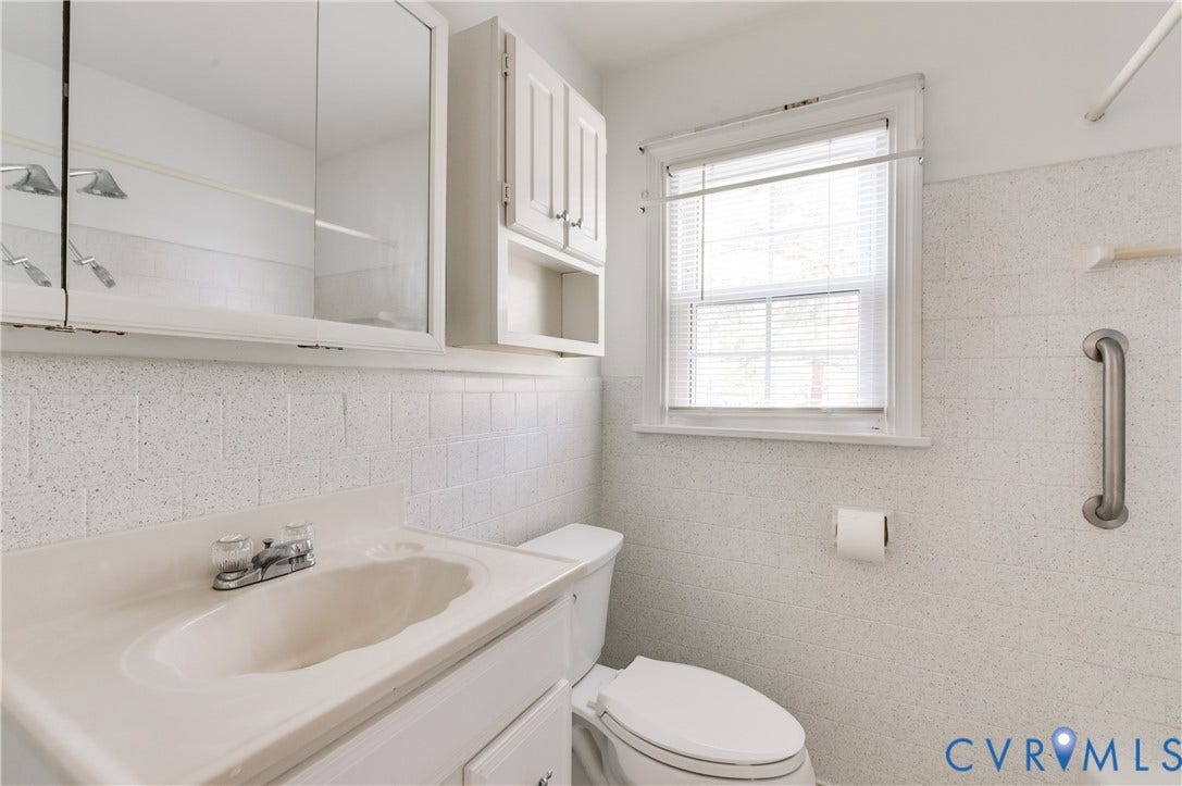 1701 Kingswood Street, Richmond, VA 23224 Bathroom featuring a single-basin vanity with an integrated countertop, wall-mounted cabinetry, a mirrored medicine cabinet, a window with horizontal blinds, and a mounted grab bar