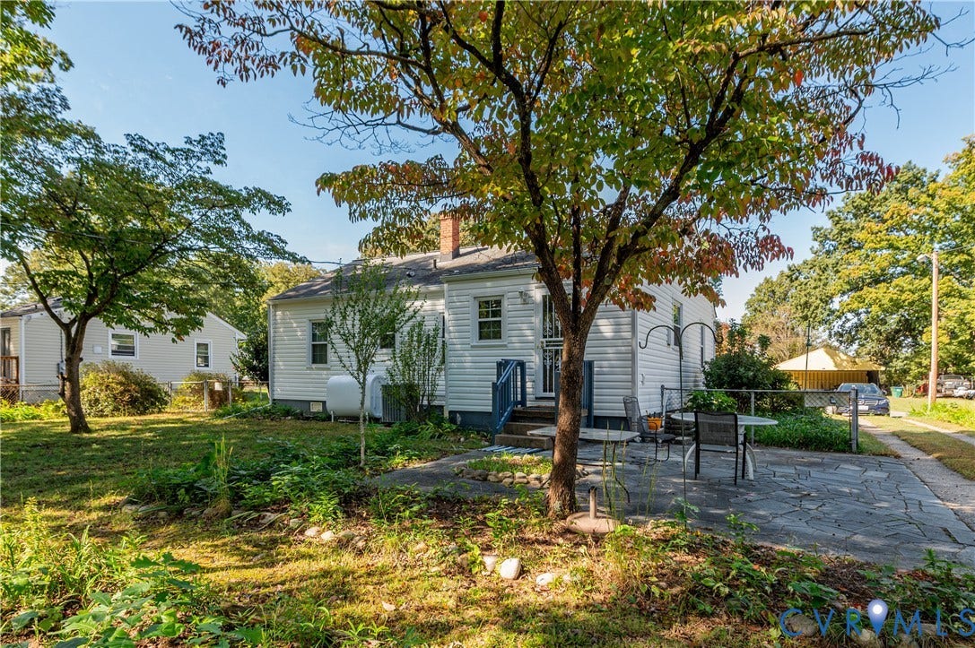 1701 Kingswood Street, Richmond, VA 23224 Exterior featuring light-colored horizontal siding, natural stone patio, mature shade trees, and chain-link perimeter fencing