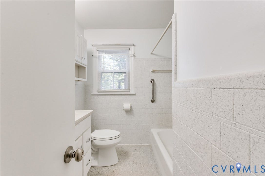 1701 Kingswood Street, Richmond, VA 23224 Bathroom featuring a white vanity cabinet, a shower-tub combination with textured tile surround, a wall-mounted grab bar, and a single-hung window