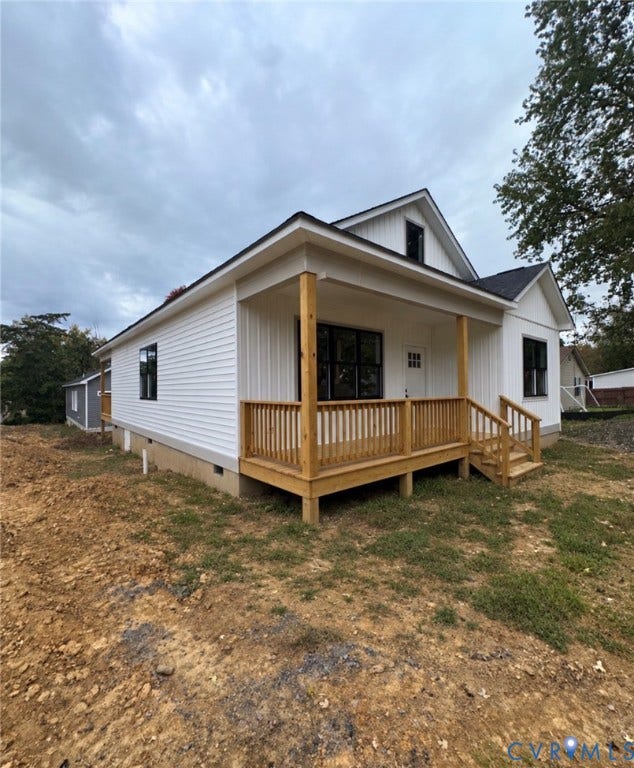 Exterior featuring white horizontal and vertical siding, dark-trimmed windows, and a raised wooden front porch with matching railing