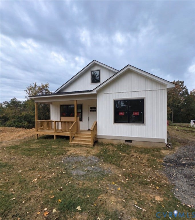 White vertical board-and-batten siding, covered front porch with wood-finish railing, and dark-trimmed exterior windows