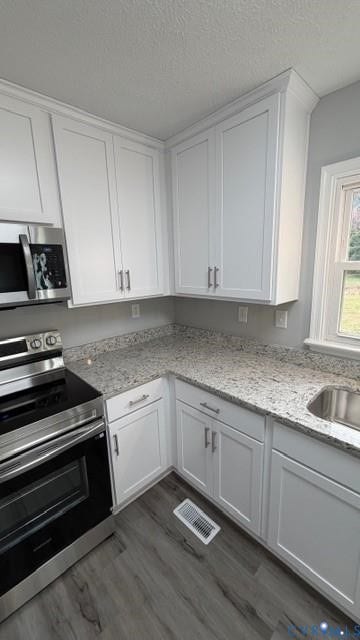White shaker-style cabinetry with crown molding, stainless steel appliances, speckled countertops, and wood-finish flooring