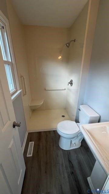 Walk-in shower with integrated seating, pedestal sink, and wood-finish flooring