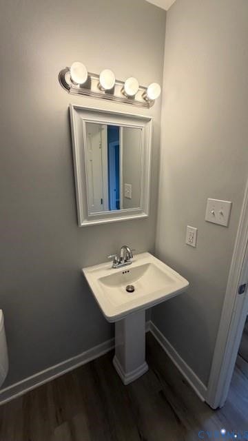 Pedestal sink with chrome faucet, framed mirror, vanity light fixture, and wood-finish flooring