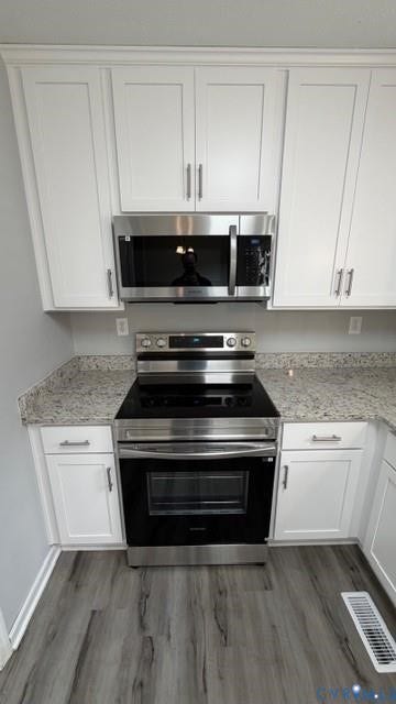 White cabinetry, stainless steel appliances, speckled countertops, and wood-finish flooring
